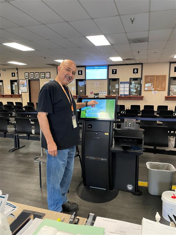 A social services employee stands with a digital kiosk used to service customers